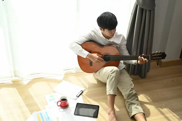 Mladý Asijský Muž Hraje Akustickou Kytaru Zatímco Sedí Podlaze Doma — Stock fotografie