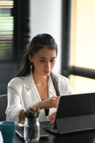 An attractive businesswoman sitting in front of computer tablet and managing her small business.