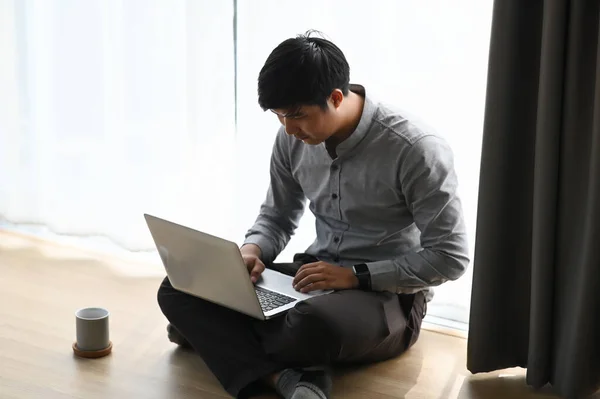 A youn businessman working on his project with laptop while sitting on floor at his room.