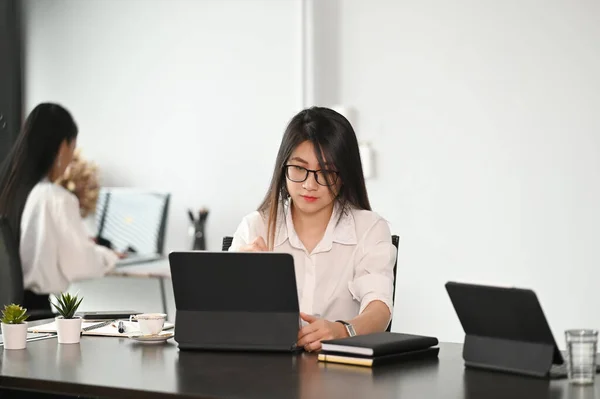 彼女のオフィスで木製のテーブルの上にノートパソコンを使用して若い女性のオフィスワーカー — ストック写真