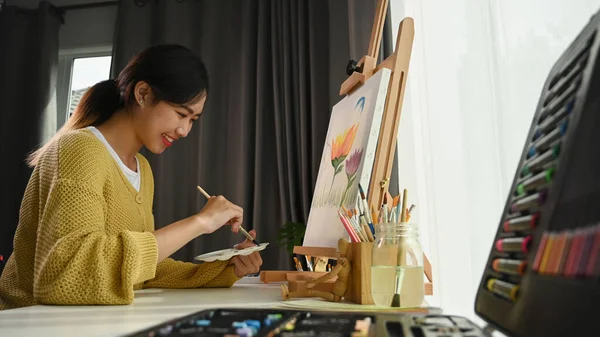 ワークショップで絵を描きながらパレットや絵筆を持つ幸せな若い女性アーティストの肖像画 — ストック写真