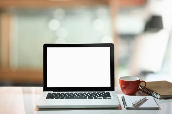 Modern work space, laptop with white screen, coffee cup and note book on white table.