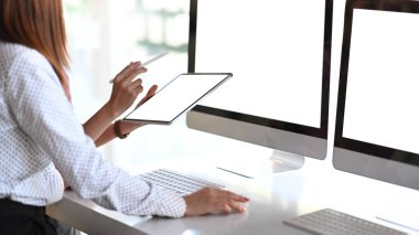 İki iş adamının kırpılmış görüntüleri, modern ofiste dijital tablet ve çoklu ekran bilgisayarla projelerine danışmanlık yapıyor..