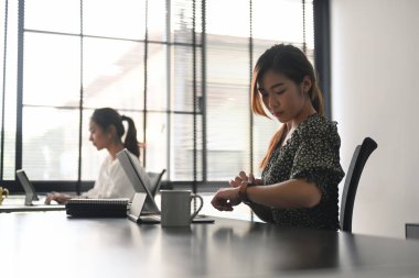 Sıradan giyinmiş iki iş kadını, modern bir ofiste aynı masada oturup tablet üzerinde çalışan iş arkadaşları..