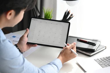 Bir iş adamının kırpılmış görüntüsü, günlük ajandası tablet bilgisayarda olan takvime bakmaktır..