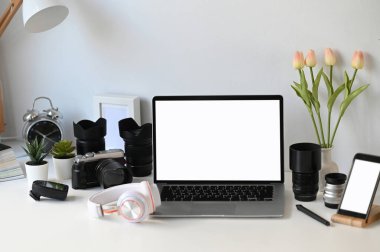 Boş ekran dizüstü bilgisayarı ve kamera aksesuarıyla grafik tasarımcı veya fotoğrafçı çalışma alanının ön görünümü.