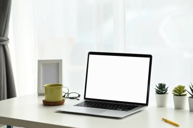 Asgari çalışma alanı boş ekran bilgisayar dizüstü bilgisayar, kaktüs ve kahve fincanını beyaz masa üzerinde oluşturur..