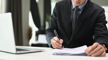 Siyah takım elbiseli kendine güvenen bir işadamı modern ofiste notlar veya mali raporlar yazıyor..
