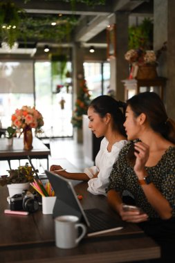 İki serbest çalışan kadın yeni fırsatlardan ve ofis masasında bilgisayar tabletleriyle çalışmaktan bahsediyor..