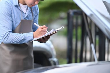 Otomobil tamircisi bir araba motorunu kontrol ediyor ve benzin istasyonundaki panoya yazı yazıyor..
