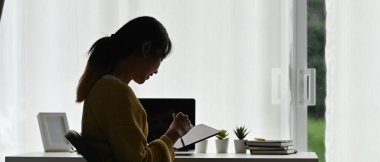 Ofisindeki cihazda çalışan ya da okuyan tablet kullanan genç bir kadının yan görüntüsü.
