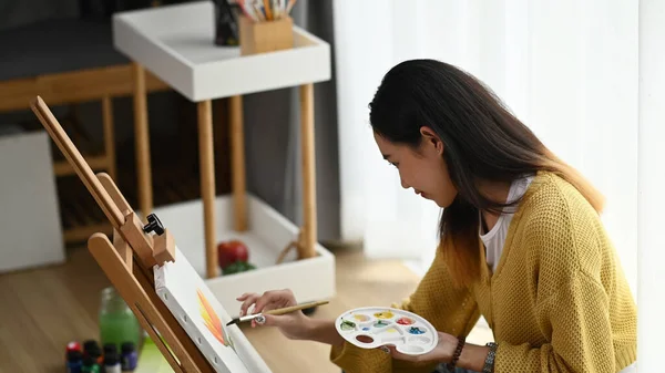 彼女のスタジオで手描きの絵にパレットを持つ若い女性アーティストの側面図 — ストック写真