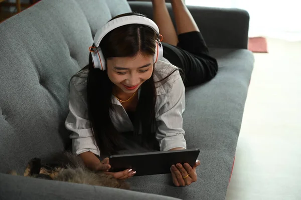 Uśmiechnięta Młoda Kobieta Siedzi Kanapie Słuchawkami Oglądając Film Tablecie Salonie — Zdjęcie stockowe