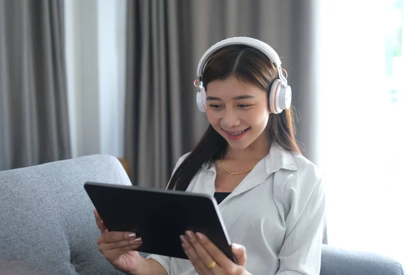Μια Χαρούμενη Γυναίκα Ακουστικά Που Κάθεται Στον Καναπέ Χρησιμοποιώντας Tablet — Φωτογραφία Αρχείου