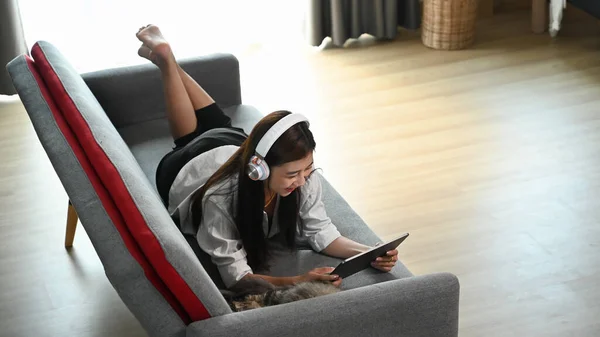 Młoda Kobieta Używa Tabletu Podczas Słuchania Muzyki Słuchawce Bezprzewodowej Leżąc — Zdjęcie stockowe
