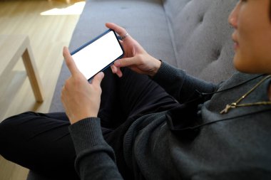 Oturma odasındaki kanepede dinlenen ve akıllı telefon kullanan mutlu genç adam..