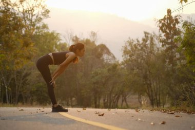 Kırsal yolda koştuktan sonra dinlenen yorgun bir kadının yan görüntüsü.