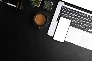 Boş ekranlı akıllı telefonun üst görünümü, dizüstü bilgisayar, defter ve siyah deri üzerine kopyalama alanı.