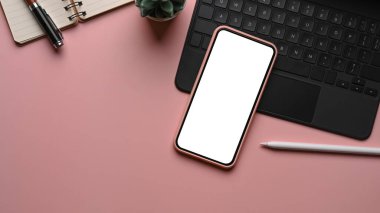 Beyaz ekranlı cep telefonu, stilus kalem, kablosuz tuş bord ve pembe pastel arka planlı defter. Kadınsı işyeri.