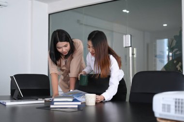 İki iş kadını mali grafikleri kontrol ediyor ve ofis masasında belgeleri inceliyor..