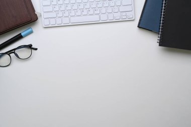 Not defteri, klavyesi, gözlüğü ve kopyalama alanı olan beyaz ofis masası.