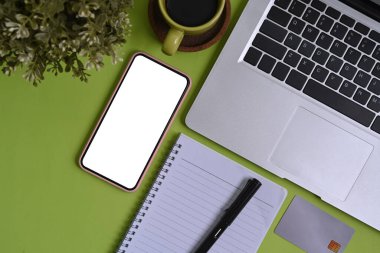 Yeşil zemin üzerinde boş ekran, not defteri, kredi kartı ve dizüstü bilgisayarı olan akıllı telefon modelinin üst görünümü.