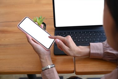 Akıllı telefon kullanan ve ofis masasında bilgisayar tabletiyle çalışan bir iş kadınını incele.