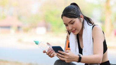 Sağlıklı genç bir kadın egzersiz sonrası ara veriyor ve akıllı telefon kullanıyor..