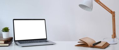 Beyaz masa üzerinde bilgisayar, bitki, kitap ve lamba gibi dizüstü bilgisayarları olan en düşük işyeri.