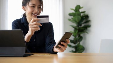 Kredi kartı tutan ve akıllı telefondan alışveriş yapan mutlu genç bir bayan..