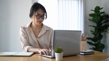 Ofiste dizüstü bilgisayarla çalışan, gözlüklü, kendine güvenen genç bir ofis çalışanı..