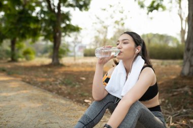 Spor yapan kadın, antrenmandan sonra dinleniyor ve plastik şişeden su içiyor..