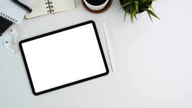 Modern iş yerinin dijital tablet, stilus kalem, kulaklık, bitki ve defterle beyaz ofis masasının üzerinde resmi..