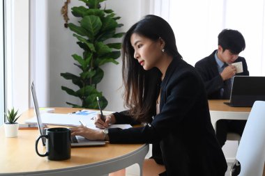 Dizüstü bilgisayarda çalışan kendine güvenen bir iş kadınının yan görünüşü ve arka planda oturan bir meslektaşımız..