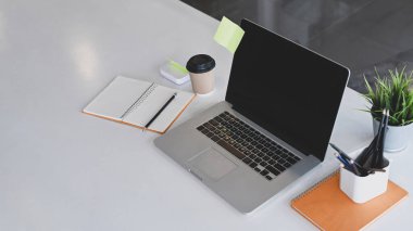 Bilgisayar, dizüstü bilgisayar, kahve fincanı ve bitki beyaz ofis masasına..