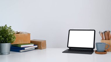 Bilgisayar tableti, ev bitkisi ve beyaz masadaki kitapları taklit eden modern işyeri.