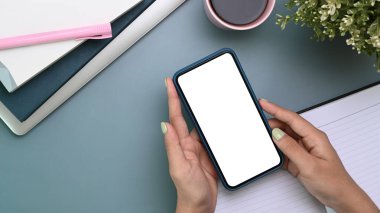 Akıllı telefon, kahve fincanı, not defteri ve koyu mavi arka planı olan tasarımcı çalışma alanının üstünde.