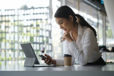 Akıllı telefon kullanan ve online ödeme işlemleri için kredi kartı tutan güzel bir iş kadını..