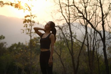 Parkta koştuktan sonra gün batımında rahatlayan çekici bir kadın..