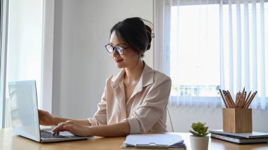 Ofiste dizüstü bilgisayarla çalışan gözlüklü, gülümseyen genç bir ofis çalışanı..
