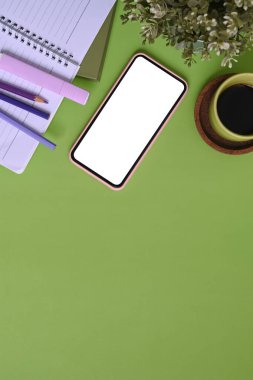Yeşil arka planda cep telefonu, kahve fincanı, bitki, defter ve kopya alanı olan tasarımcı işyeri.
