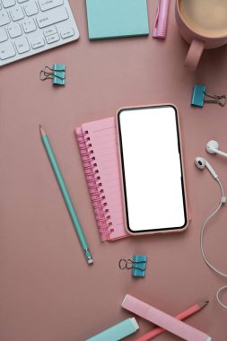 Akıllı telefon defteri ve pembe arka planda ofis malzemeleri olan kadınsı bir iş yeri..