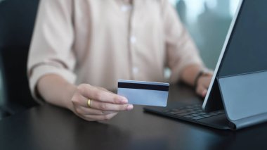 İnternet üzerinden veya boş ofis masasında internet bankacılığı yapmak için bilgisayar tableti ve kredi kartı kullanan genç bir kadın..
