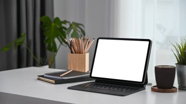 Bilgisayar tableti, defter, kahve fincanı ve bitkiyle rahat bir iş yeri..