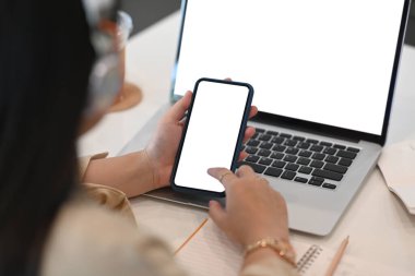 Bilgisayarın önünde oturan ve cep telefonu kullanan genç bir ofis çalışanı..