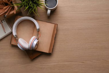 Kahve fincanı, kırtasiye, kulaklık, bitki, defter ve ahşap arka planda kopyalama alanı olan klasik işyeri manzarasının üstünde..