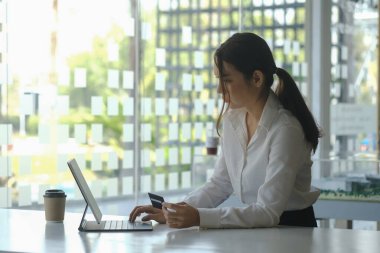 Kredi kartı tutan ve bilgisayar tableti kullanan genç bir kadının yan görünümü online alışveriş veya çevrimiçi ödeme işlemi.