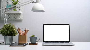 Bilgisayarlı ofis masası, kahve fincanı, dijital tablet, ev bitkisi ve kalem tutacağı beyaz masada..