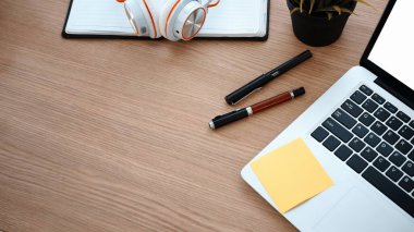 Bilgisayar dizüstü bilgisayarı, kalemler, telefon ve defter ahşap ofis masasında..