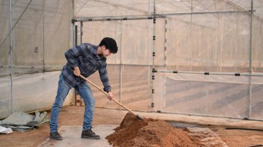 Genç çiftçi serada kürekle toprağı kazıyor..